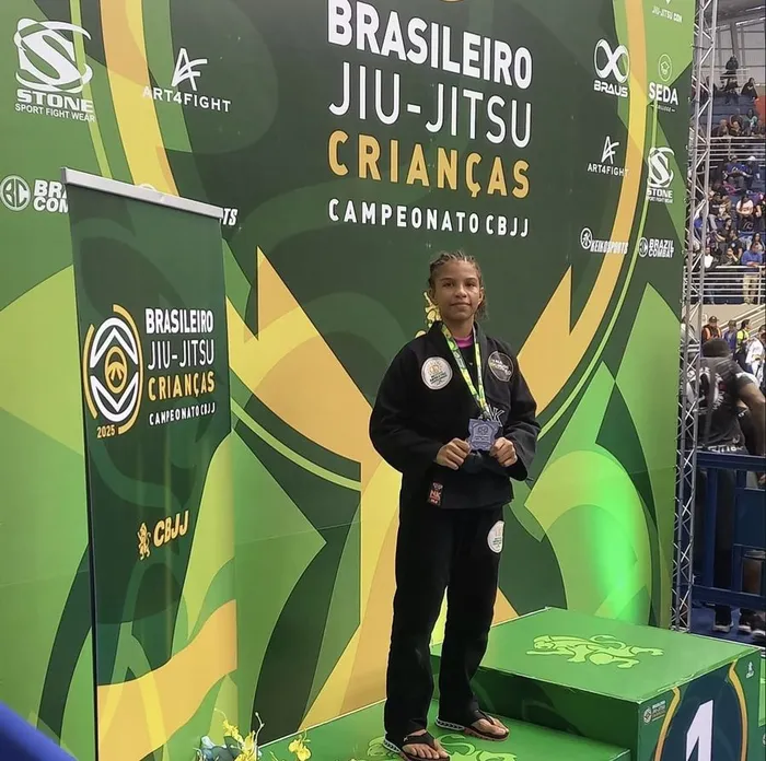 Emanuelly Sophia em pé no pódio do Brasileiro de Jiu-Jitsu Crianças, de quimono preto e medalha
