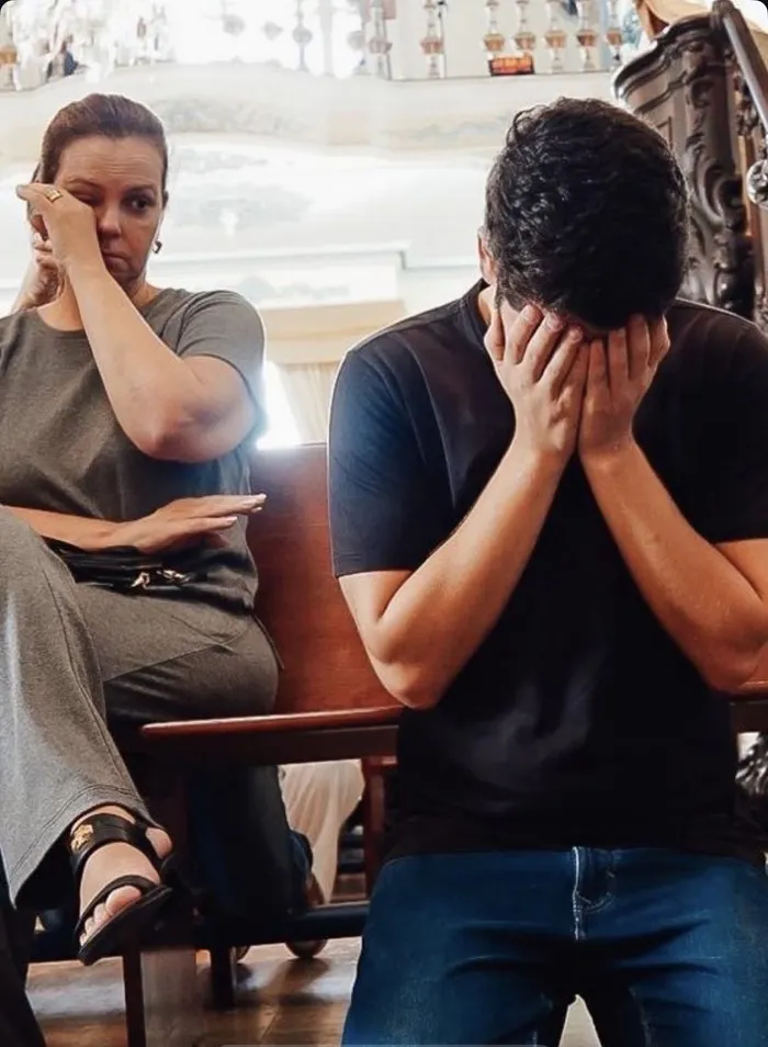 João Drumond, emocionado, com o rosto entre as mãos, sentado num banco de igreja